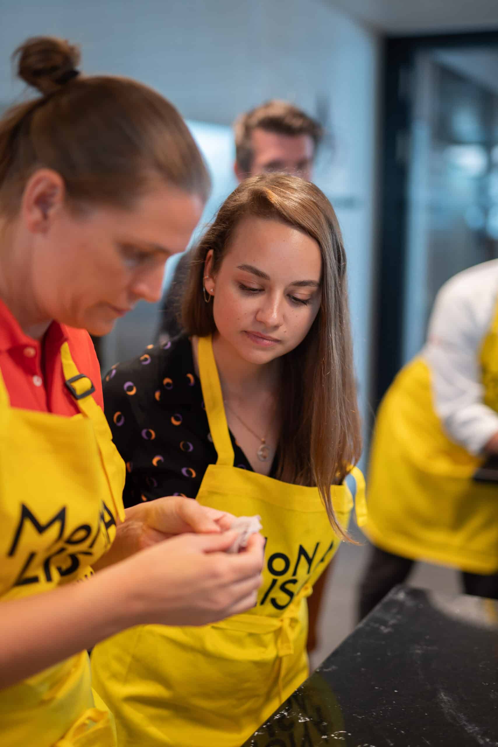 Teilnehmer zwei Frauen gelbe Schürtze Küche Workshop Mona Lisa Chocholate Academy Eventfotografie Zürich Schweiz BeLighted